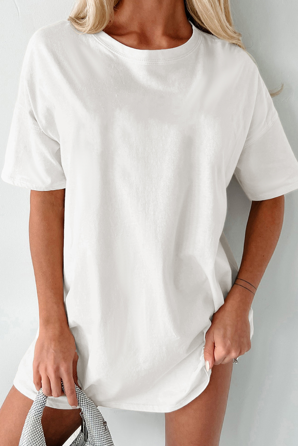 Add a timeless piece to your wardrobe with this Women's White Solid Color Round Neck Basic Tunic T-Shirt. This essential tee is perfect for everyday wear, featuring short sleeves for a casual and versatile look. The comfortable crew neck adds a timeless appeal to the tunic, while the tunic length offers a flattering and stylish silhouette. Made from a blend of 95% cotton and 5% elastane, this t-shirt ensures comfort and durability. The solid white color provides a clean and classic aesthetic, making it suitable for various occasions. Whether you're running errands or relaxing at home, this basic tunic tee is a must-have for effortless style and comfort. Pair it with your favorite jeans or leggings for a laid-back yet chic ensemble. - Detail View 4 Add a timeless piece to your wardrobe with this Women's White Solid Color Round Neck Basic Tunic T-Shirt. This essential tee is perfect for everyday wear, featuring short sleeves for a casual and versatile look. The comfortable crew neck adds a timeless appeal to the tunic, while the tunic length offers a flattering and stylish silhouette. Made from a blend of 95% cotton and 5% elastane, this t-shirt ensures comfort and durability. The solid white color provides a clean and classic aesthetic, making it suitable for various occasions. Whether you're running errands or relaxing at home, this basic tunic tee is a must-have for effortless style and comfort. Pair it with your favorite jeans or leggings for a laid-back yet chic ensemble. - Detail View 4