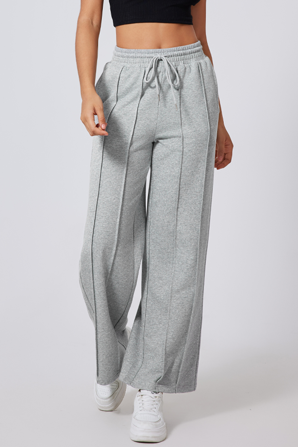 Elevate your athleisure style with these Women's Gray Seamed Drawstring High Waist Wide Leg Sweatpants. The stylish seamed detailing adds a trendy touch to the design, while the adjustable drawstring high waist offers a customized and comfortable fit. The wide leg silhouette provides a relaxed and comfortable feel, making these sweatpants perfect for daily activities and exercises. Made from a premium blend of 65% polyester and 35% cotton, these sweatpants ensure durability and breathability. Available in a versatile gray color, they can easily complement any style and outfit. Whether you're hitting the gym, going for a run, or simply lounging at home, these sweatpants are a must-have addition to your activewear collection. - Detail View 4 Elevate your athleisure style with these Women's Gray Seamed Drawstring High Waist Wide Leg Sweatpants. The stylish seamed detailing adds a trendy touch to the design, while the adjustable drawstring high waist offers a customized and comfortable fit. The wide leg silhouette provides a relaxed and comfortable feel, making these sweatpants perfect for daily activities and exercises. Made from a premium blend of 65% polyester and 35% cotton, these sweatpants ensure durability and breathability. Available in a versatile gray color, they can easily complement any style and outfit. Whether you're hitting the gym, going for a run, or simply lounging at home, these sweatpants are a must-have addition to your activewear collection. - Detail View 4